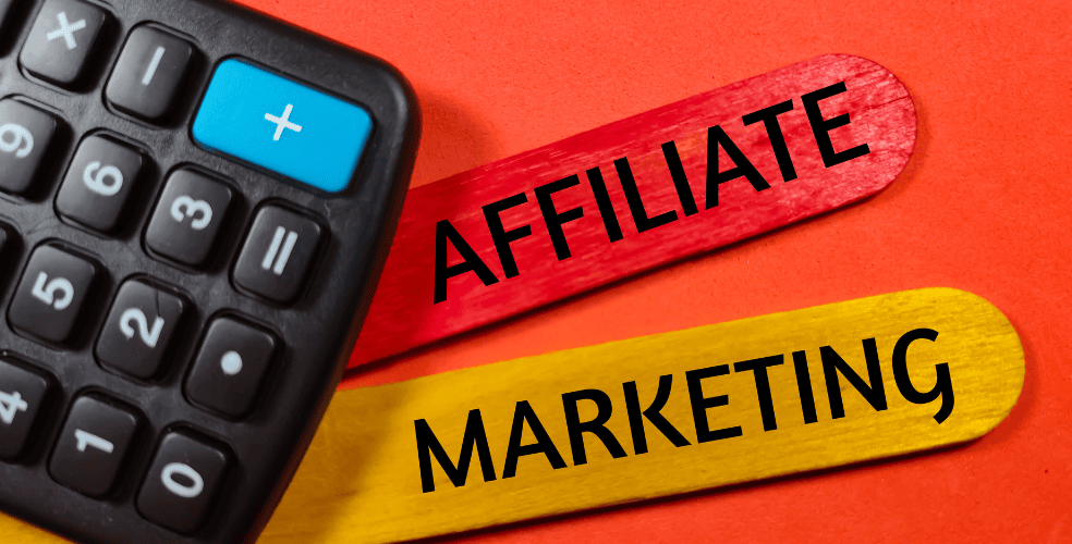 Una calcolatrice nera su sfondo rosso con due spatole in legno incrociate con le parole 'AFFILIATE MARKETING' in caratteri neri che enfatizzano le strategie di monetizzazione attraverso l'affiliazione per i blogger.