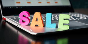 Lettere colorate tridimensionali che formano la parola 'SALE' sul laptop con sfondo sfocato di un sito e-commerce, riflettendo il processo di design di una pagina di vendita accattivante per il web.
