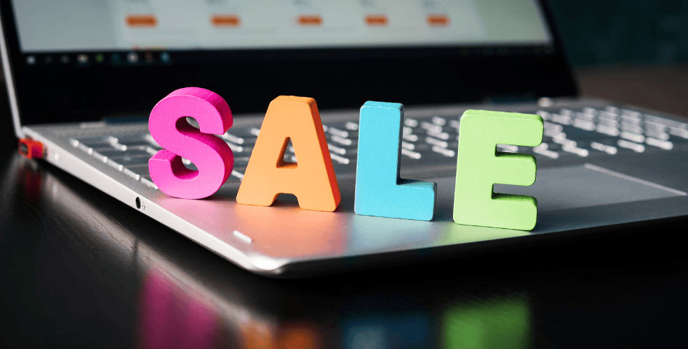 Lettere colorate tridimensionali che formano la parola 'SALE' sul laptop con sfondo sfocato di un sito e-commerce, riflettendo il processo di design di una pagina di vendita accattivante per il web.