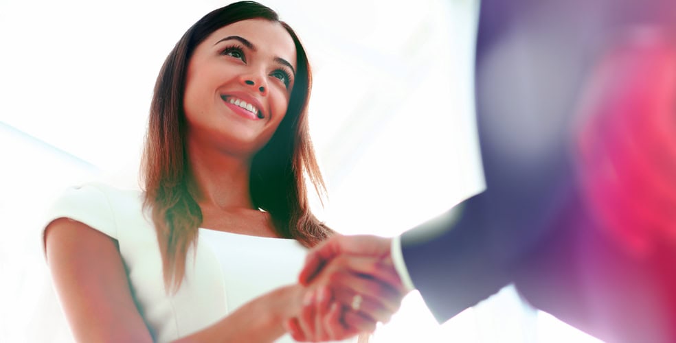 Donna che stringe la mano a un uomo d'affari, sorridente, in un ambiente luminoso, rappresentando l'importanza del personal branding per attrarre nuovi clienti.