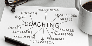 Mappa concettuale del coaching su un foglio, circondata da occhiali, penna e tazza di caffè, rappresentando il ruolo del coaching nella crescita professionale.