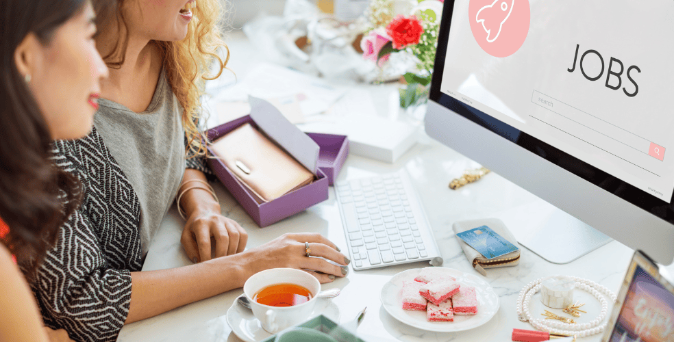 Due donne che cercano lavoro online su un computer desktop, sorridendo e discutendo le opportunità.