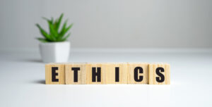 Parola 'ETHICS' composta da blocchi di legno, con una pianta in vaso sullo sfondo sfocato, rappresentando il concetto di etica nel web design.