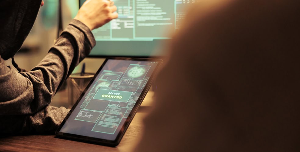 Persona in abbigliamento casual che lavora su un tablet con un display che mostra 'access granted', con uno schermo di computer sullo sfondo, rappresentando l'integrazione di front-end e back-end nel web design.