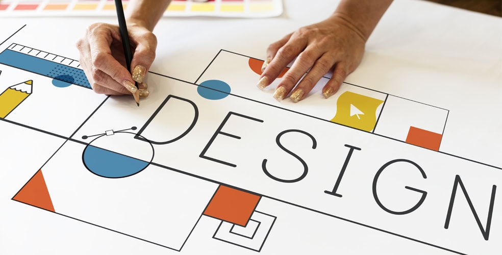 Persona che disegna la parola 'Design' su un foglio con vari elementi geometrici e colori vivaci, rappresentando l’unione tra design tradizionale e web design moderno.