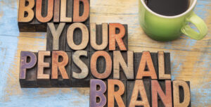 Parole 'Build Your Personal Brand' disposte con caratteri in legno su un tavolo, affiancate da una tazza di caffè verde, simboleggiando il concetto di costruzione di un personal branding.