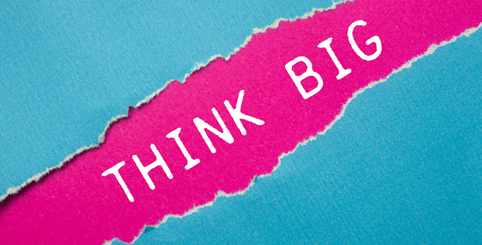 Frase 'Think Big' incisa su carta strappata rosa e sfondo azzurro, rappresentando il pensiero creativo e strategico nella scrittura di guest post.