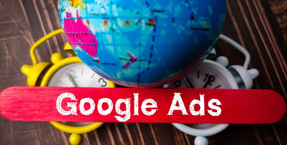 Globo terrestre su sfondo di sveglie colorate, accompagnato da scritta 'Google Ads', rappresentando la dimensione globale delle campagne pubblicitarie.