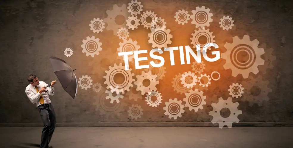 Immagine concettuale orizzontale: uomo in camicia bianca e cravatta gialla, spaventato, si protegge con un ombrello mentre guarda una parete scura su cui esplode una nuvola di ingranaggi sovrapposti color arancio con la scritta grande “TESTING”; metafora visiva della complessità dei test software, regressione e automazione che travolgono il team.