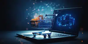 Immagine concettuale di un carrello della spesa digitale posizionato sopra la tastiera di un laptop, con scatole luminose all’interno e particelle di luce che fluttuano nell’aria, simboleggiando l’e-commerce, la digitalizzazione delle vendite e l’innovazione tecnologica nel commercio online.