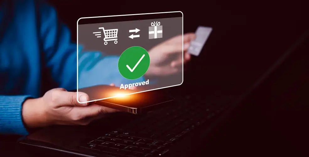 Foto concettuale sull’usabilità del checkout: una persona tiene uno smartphone sopra la tastiera di un laptop mentre con l’altra mano mostra una carta di pagamento; davanti allo schermo appare un’interfaccia trasparente in stile digitale con icone di carrello e regalo e un grande segno di spunta verde “Approved”, che comunica pagamento approvato, esperienza d’acquisto fluida e conversione nell’e-commerce.